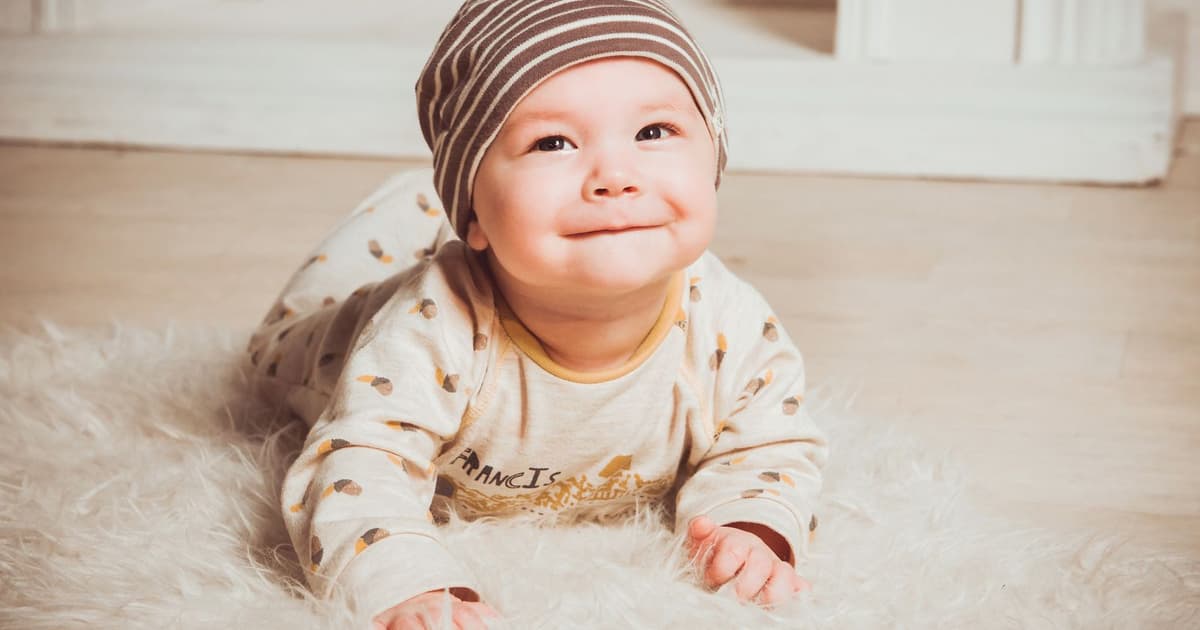 Bebis i hatt som ligger på magen på en fluffig matta